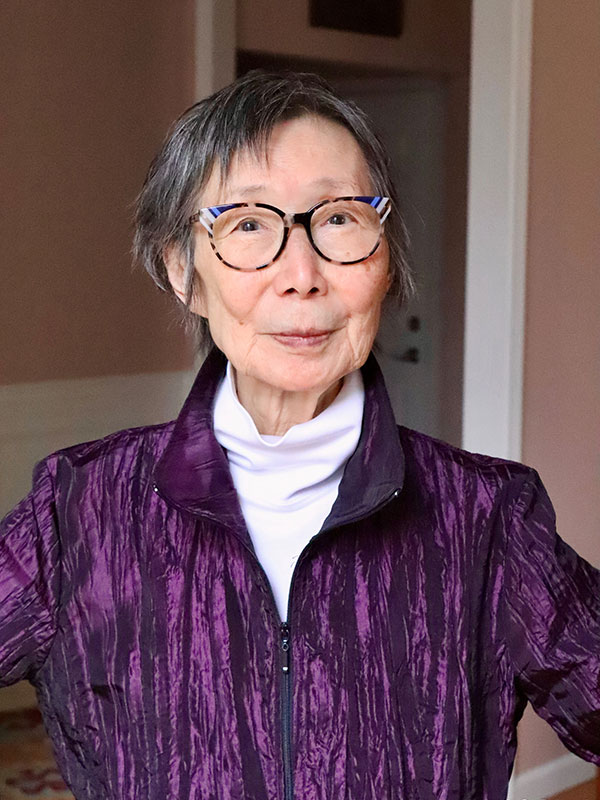 A headshot of Professor Emerita Sumie Jones, who wears a purple zipper jacket and a white shirt.